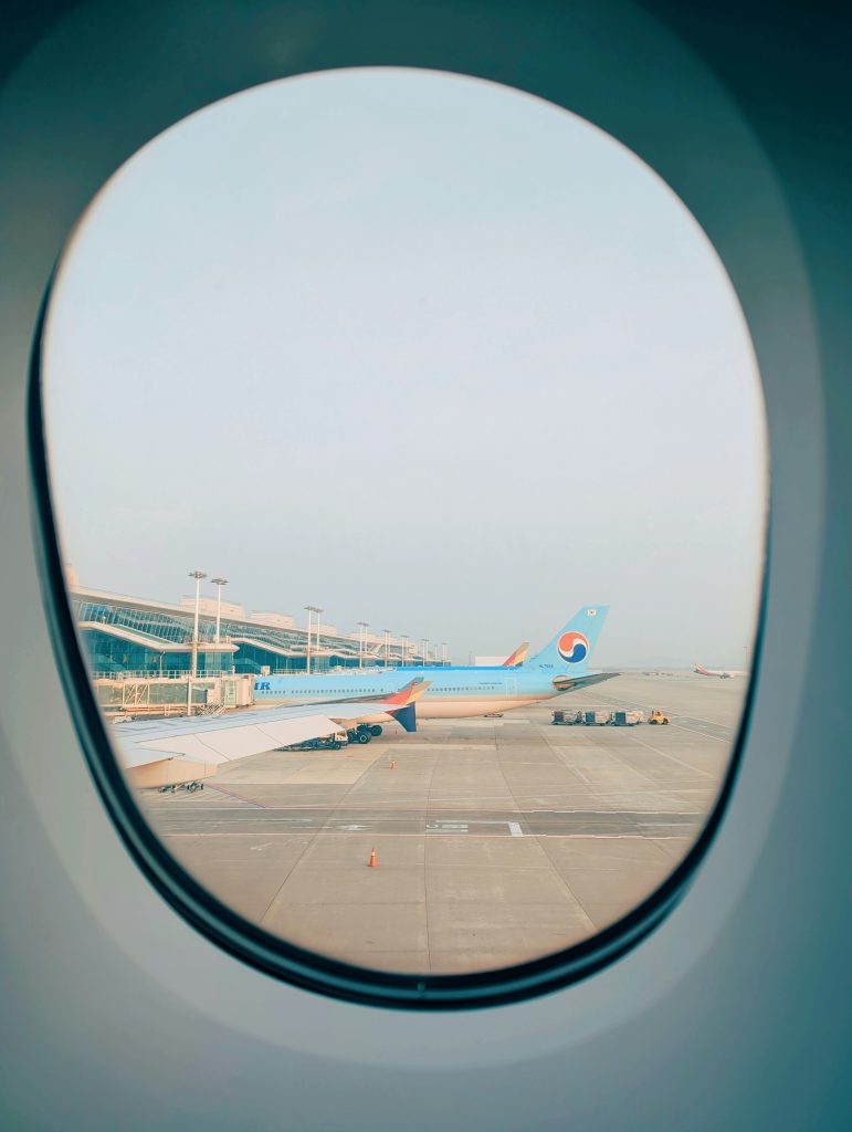 View of Incheon Airport through an airplane window, with Korean Air and Asiana aircraft parked at the gates